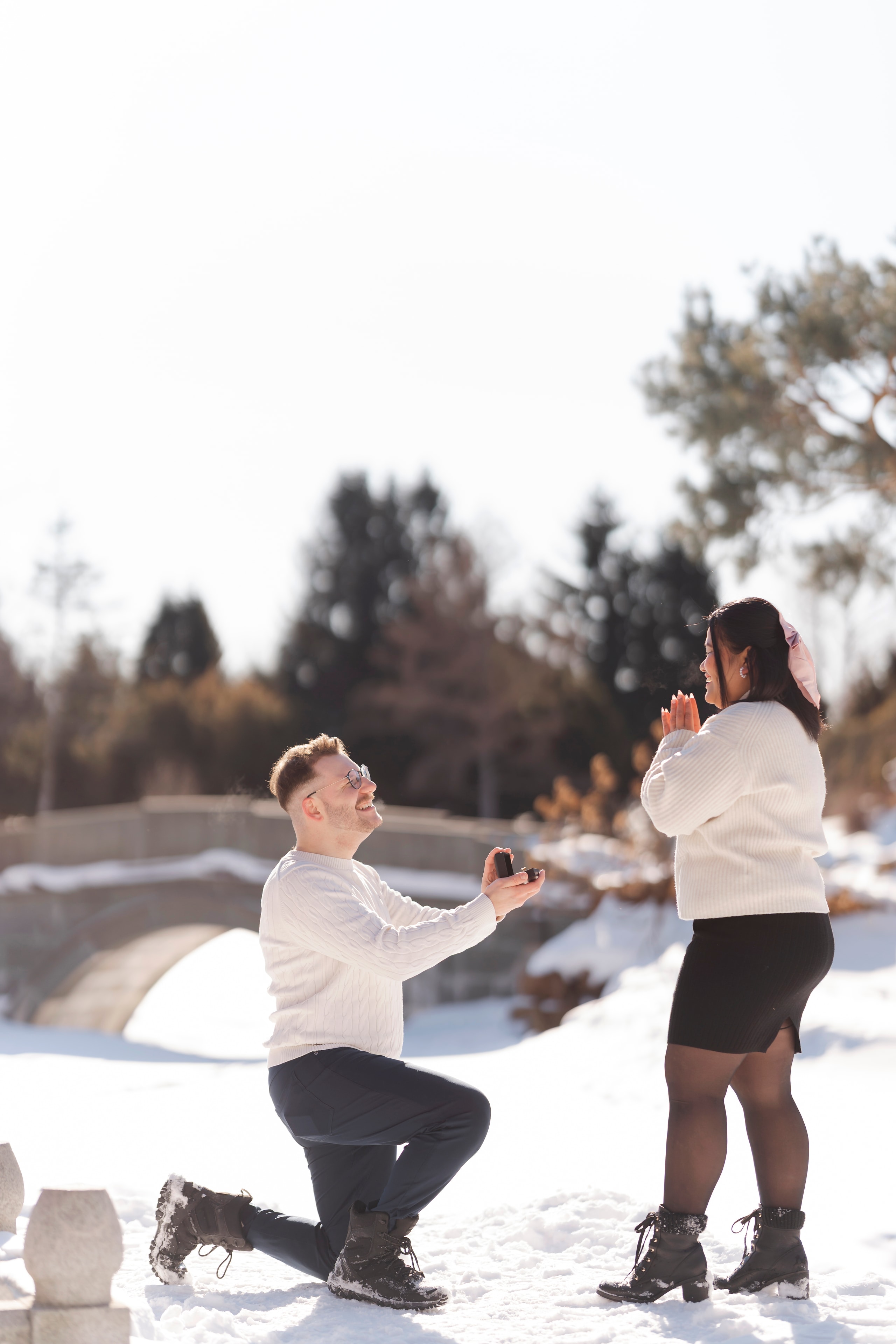 man on one knee proposing to woman in snowy park winter engagement