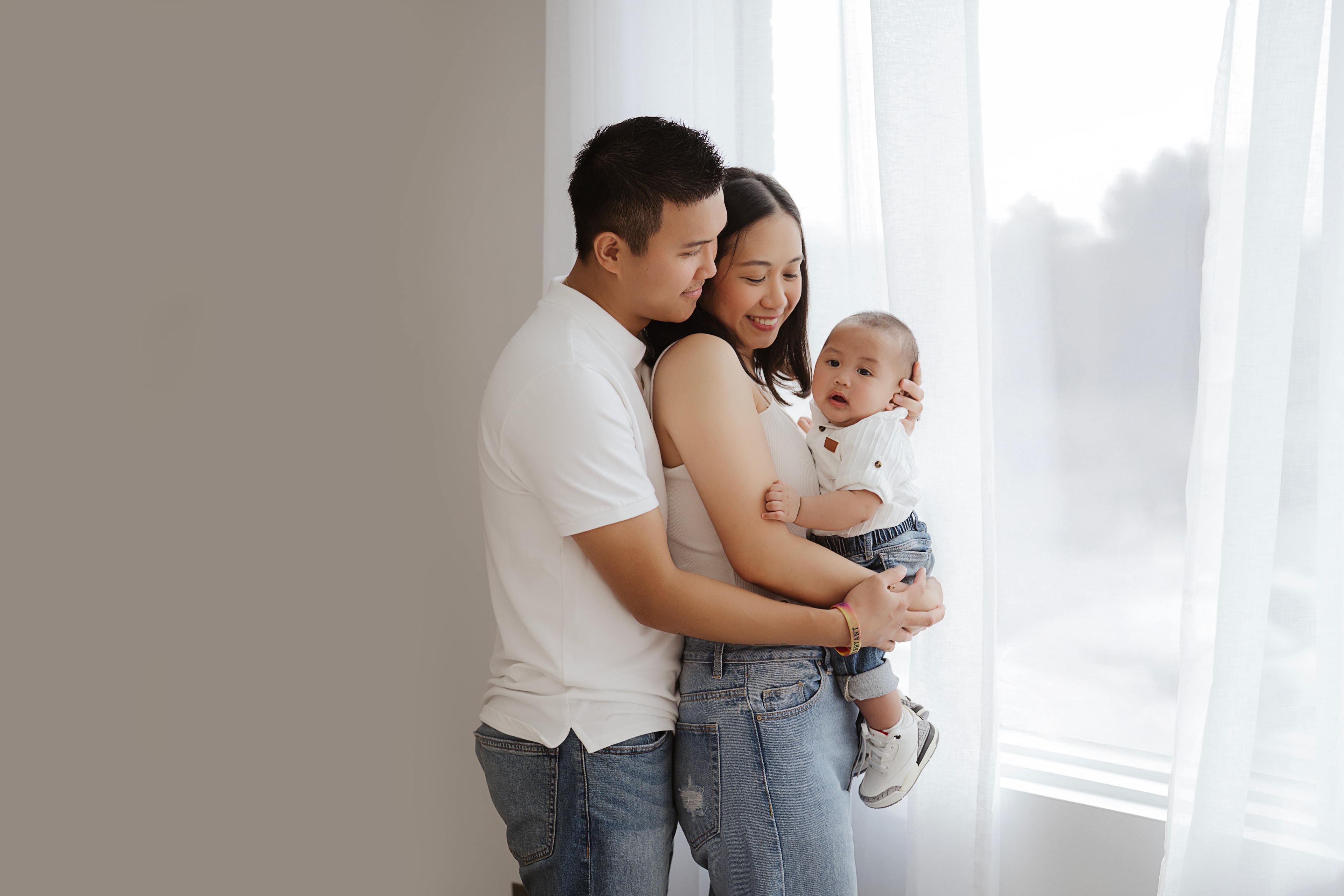 young couple holding baby by window natural light studio