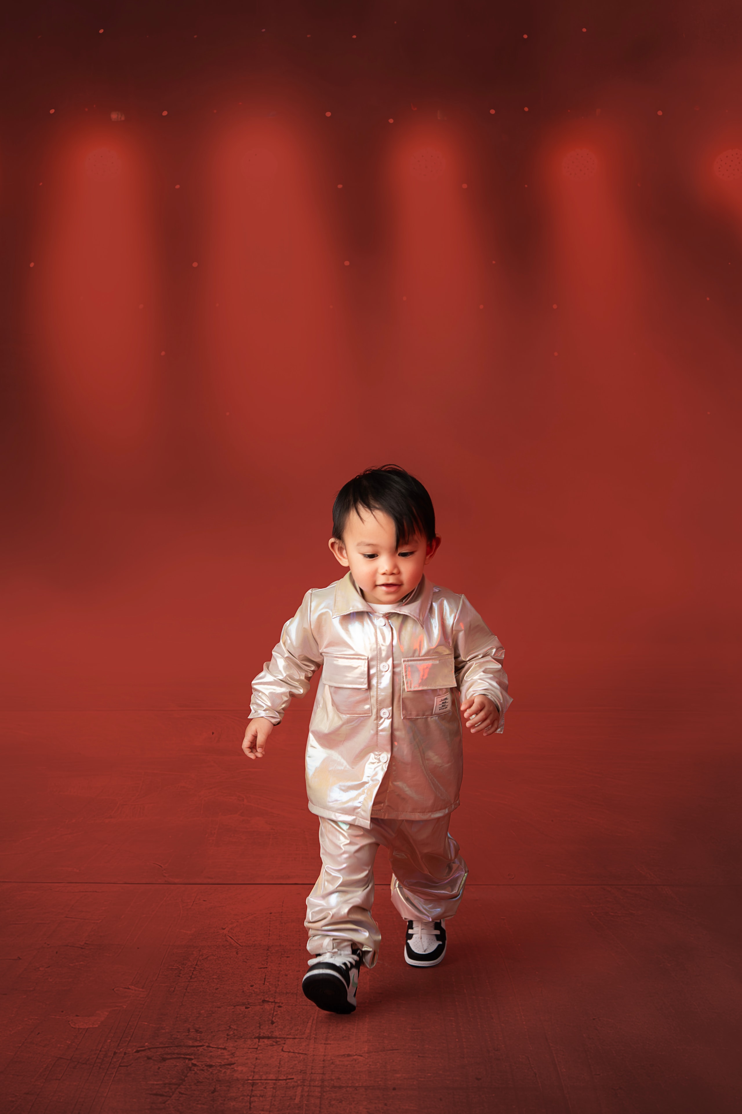toddler boy in silver outfit walking red background studio portrait