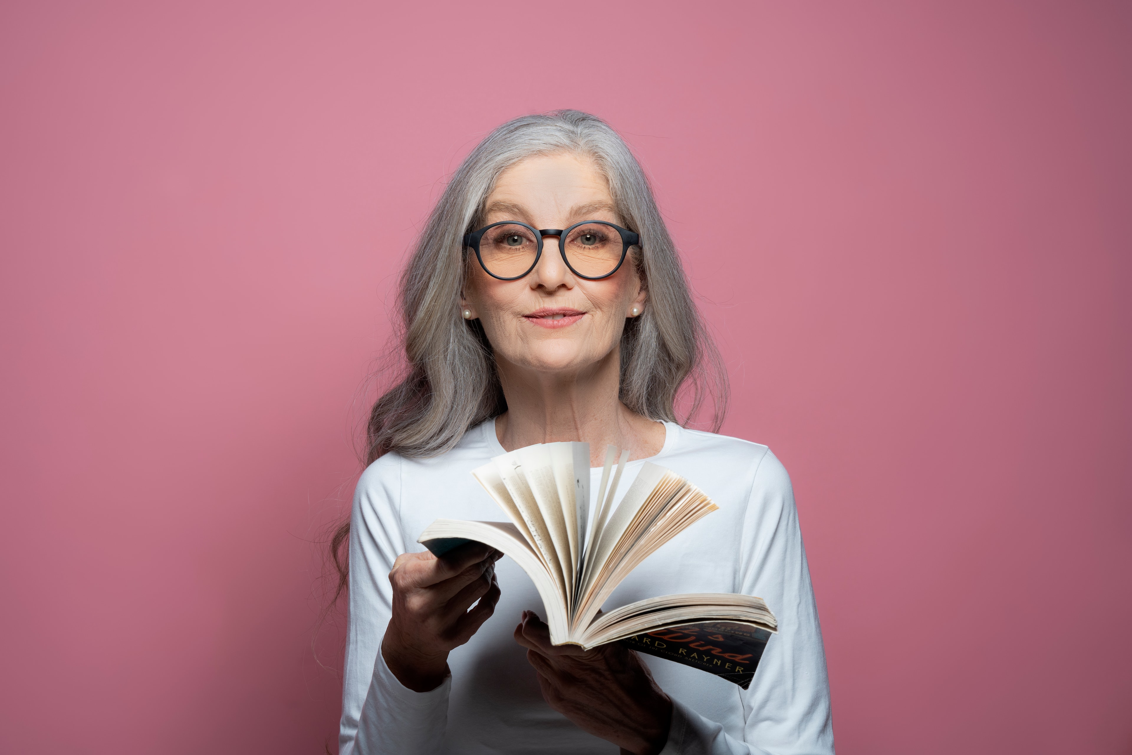 woman with gray hair holding open book pink background portrait product photography