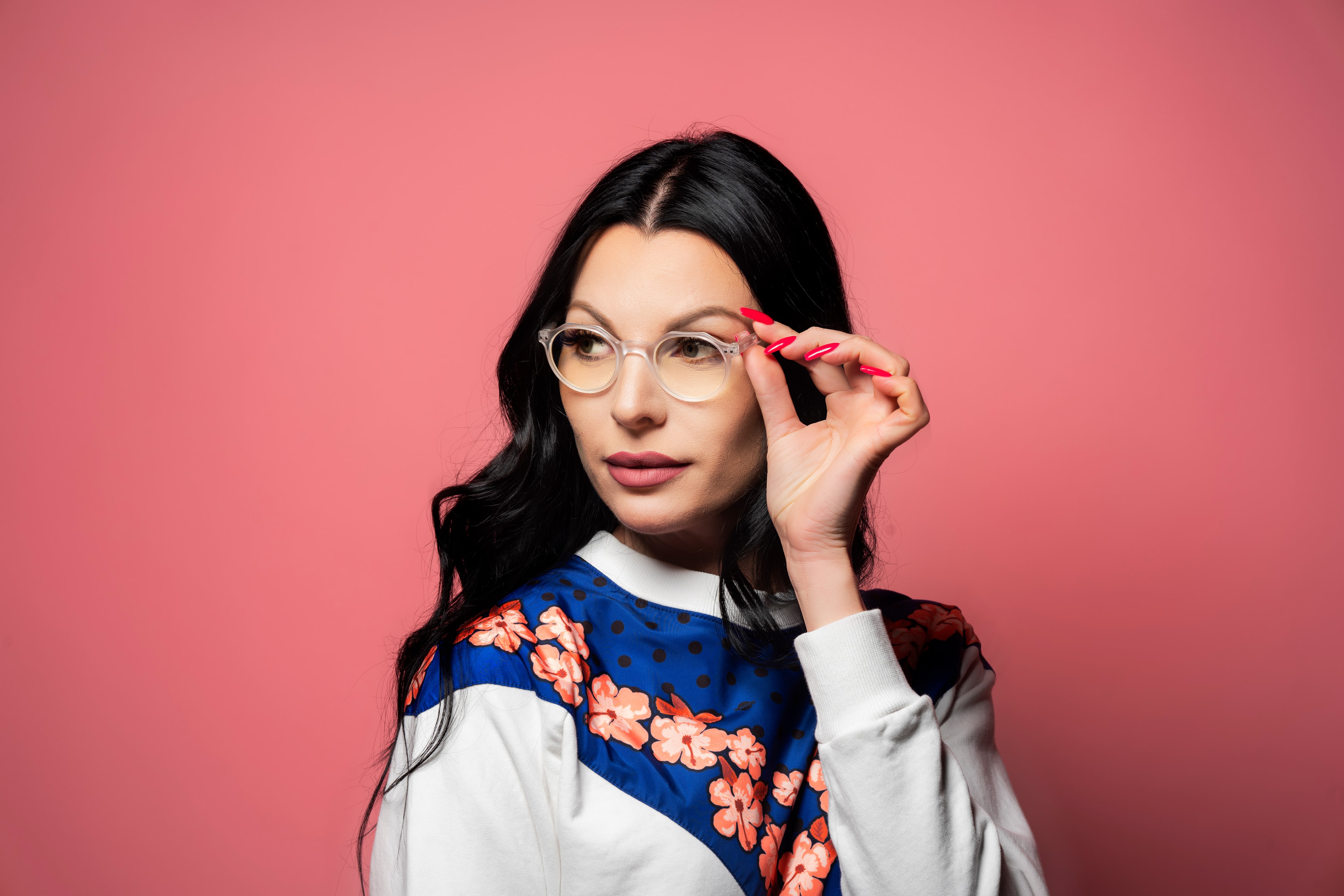 woman with dark hair adjusting glasses pink background product portrait photography