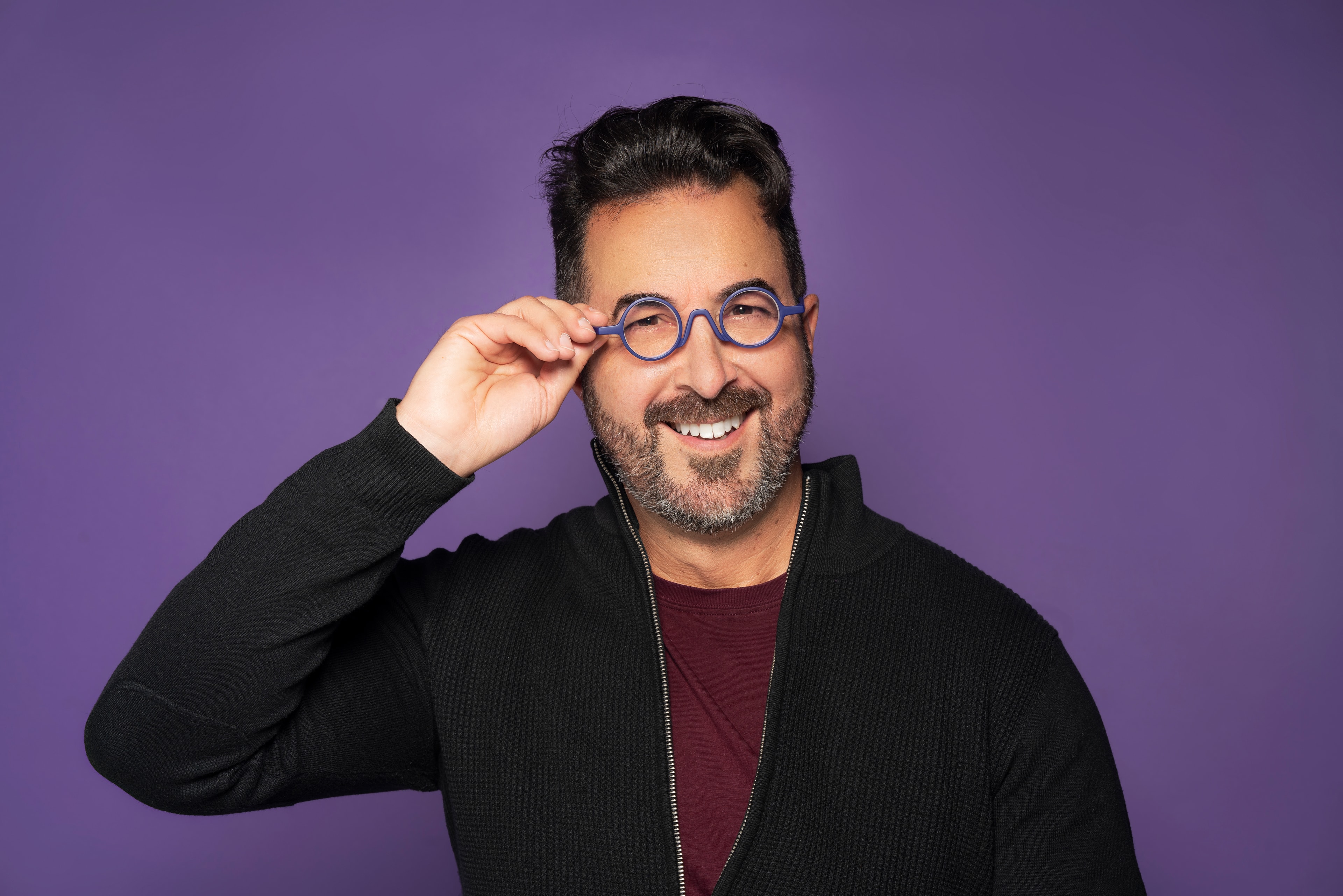 man smiling adjusting round glasses purple background product portrait photography