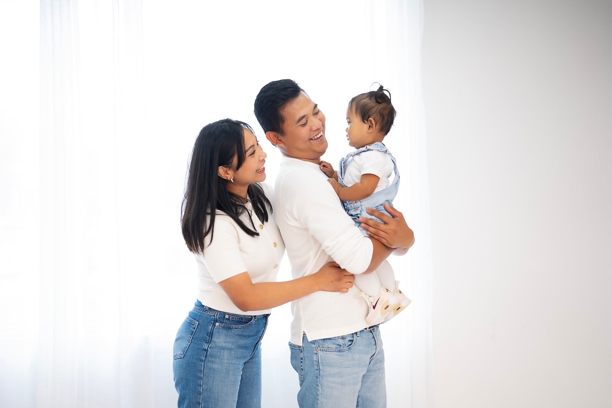 parents laughing holding baby girl white studio portrait